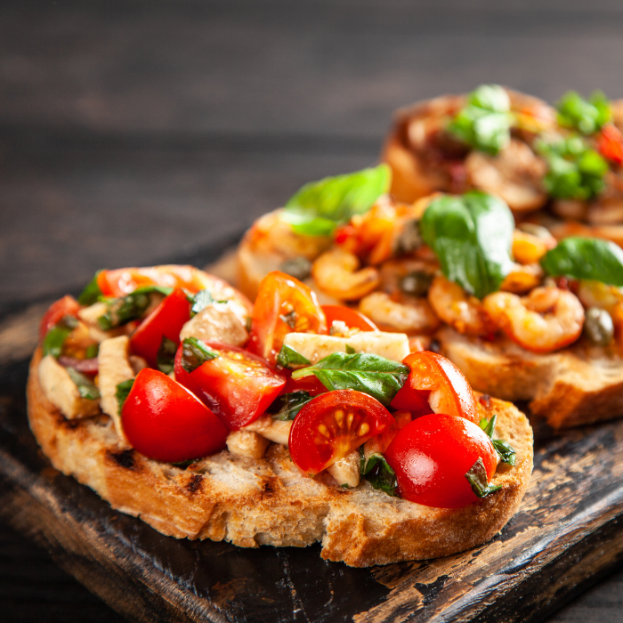 Grilled bread crostini piled with cherry tomatoes, basil and greens on a dark board