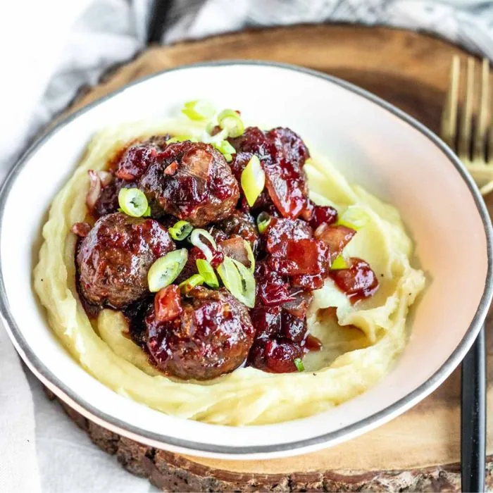 Turkey meatballs glazed in cranberry sauce on mashed potato, scattered with spring onion