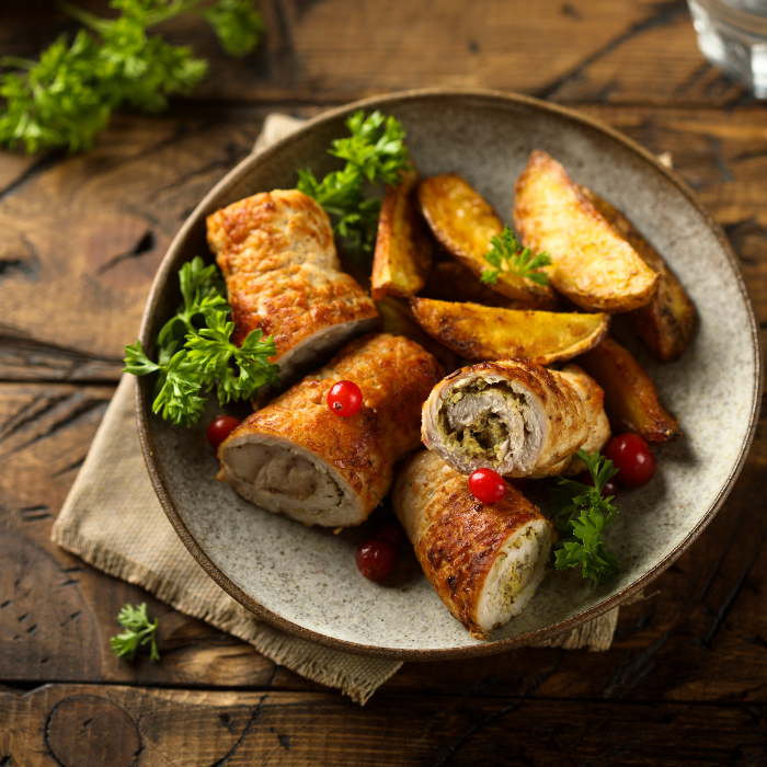 Stuffed turkey roulades with roasted potato wedges, parsley and cranberries on a stoneware plate