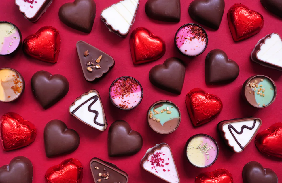 Chocolate hearts, red foil-wrapped hearts and filled bonbons scattered on a deep red background