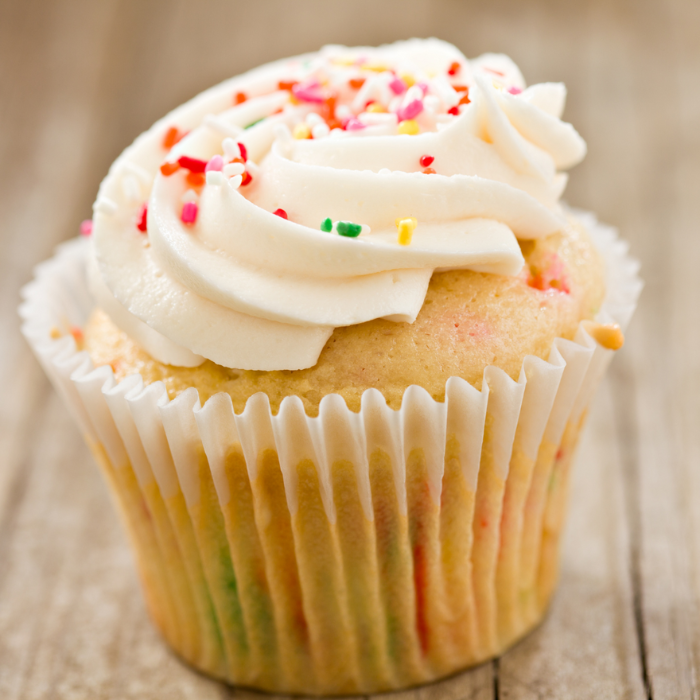Vanilla cupcake topped with a swirl of buttercream and rainbow sprinkles in a paper liner
