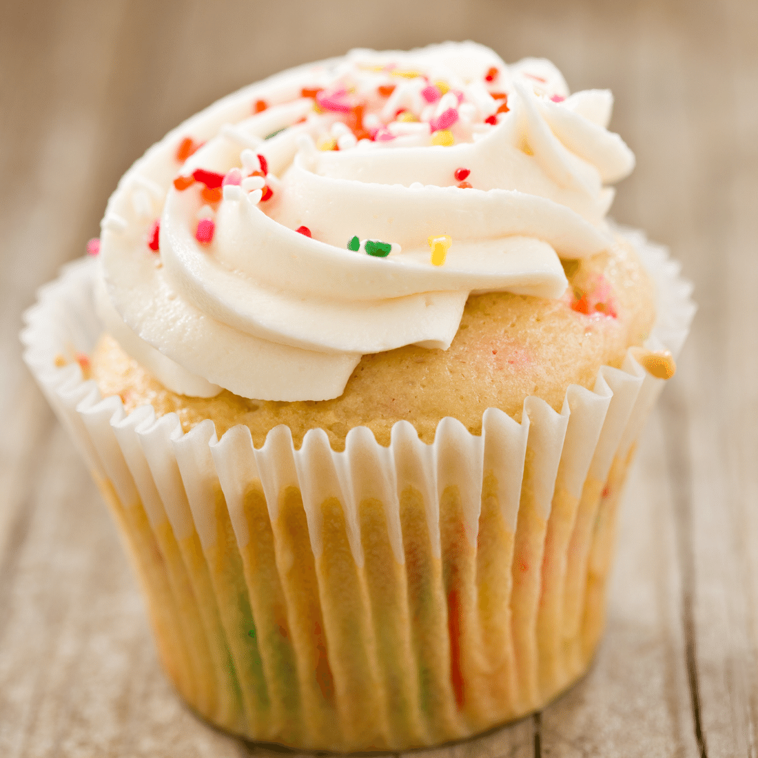 Vanilla cupcake topped with a swirl of white buttercream and rainbow sprinkles