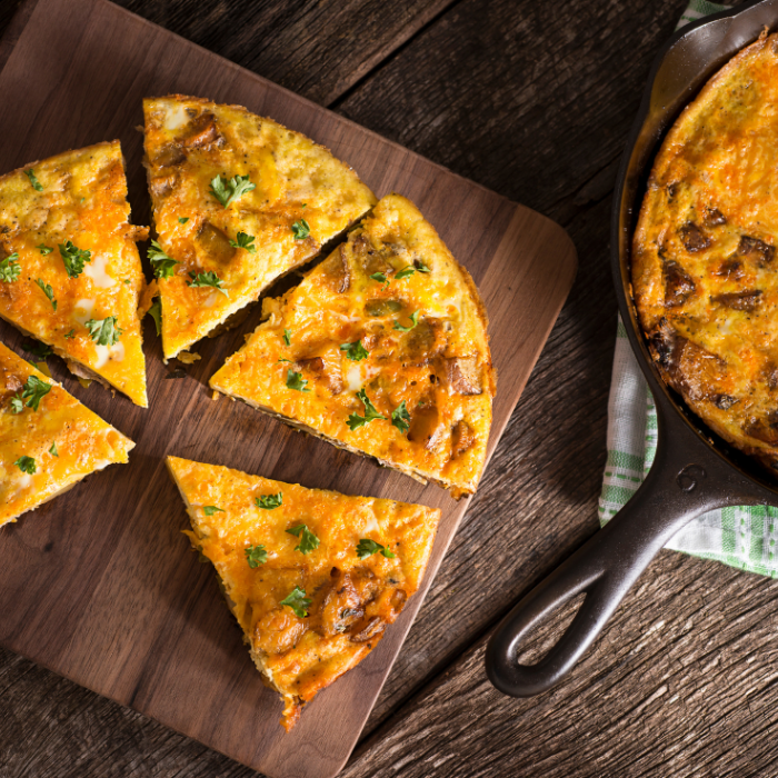 Vegetable frittata cut into wedges on a wooden board next to the cast iron skillet it baked in