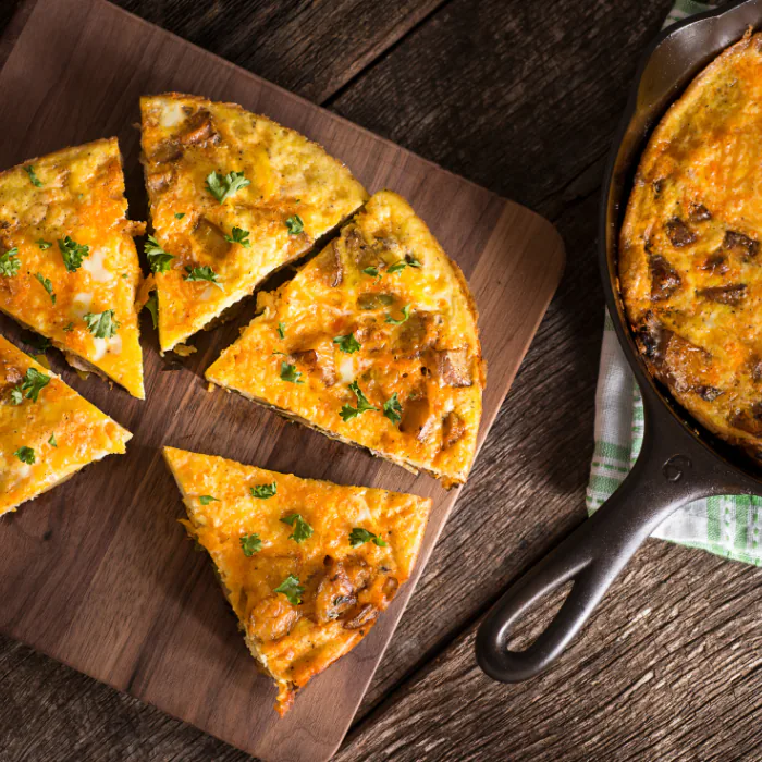 Vegetable frittata cut into wedges on a wooden board next to the cast iron skillet it baked in