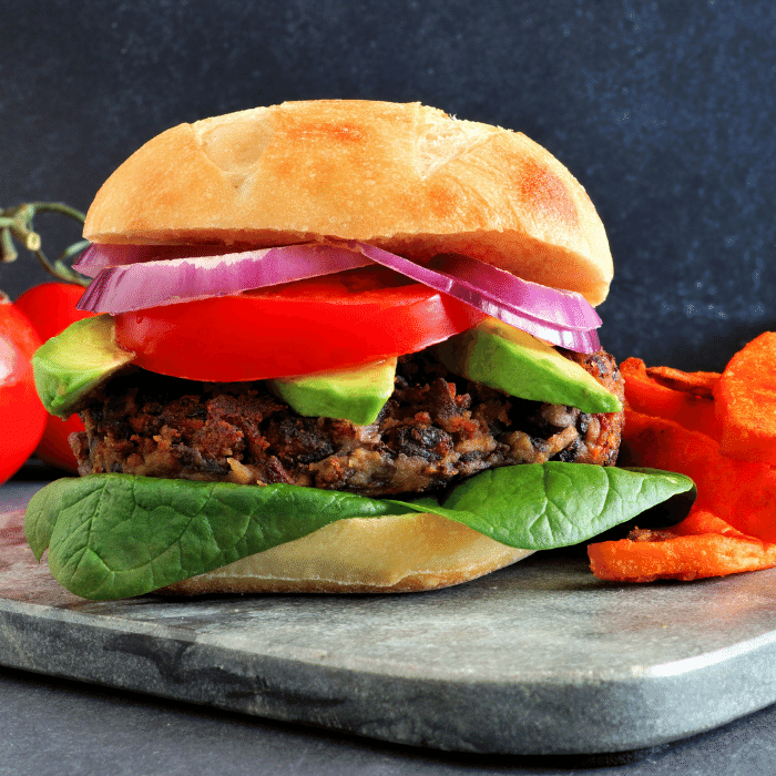 Plant-based burger stacked with avocado, tomato, red onion and spinach, served with sweet potato fries