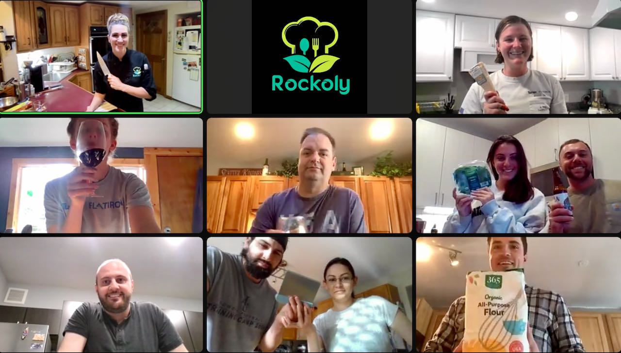 Nine coworkers on a video call holding up bags of flour and mixing bowls during a cooking class