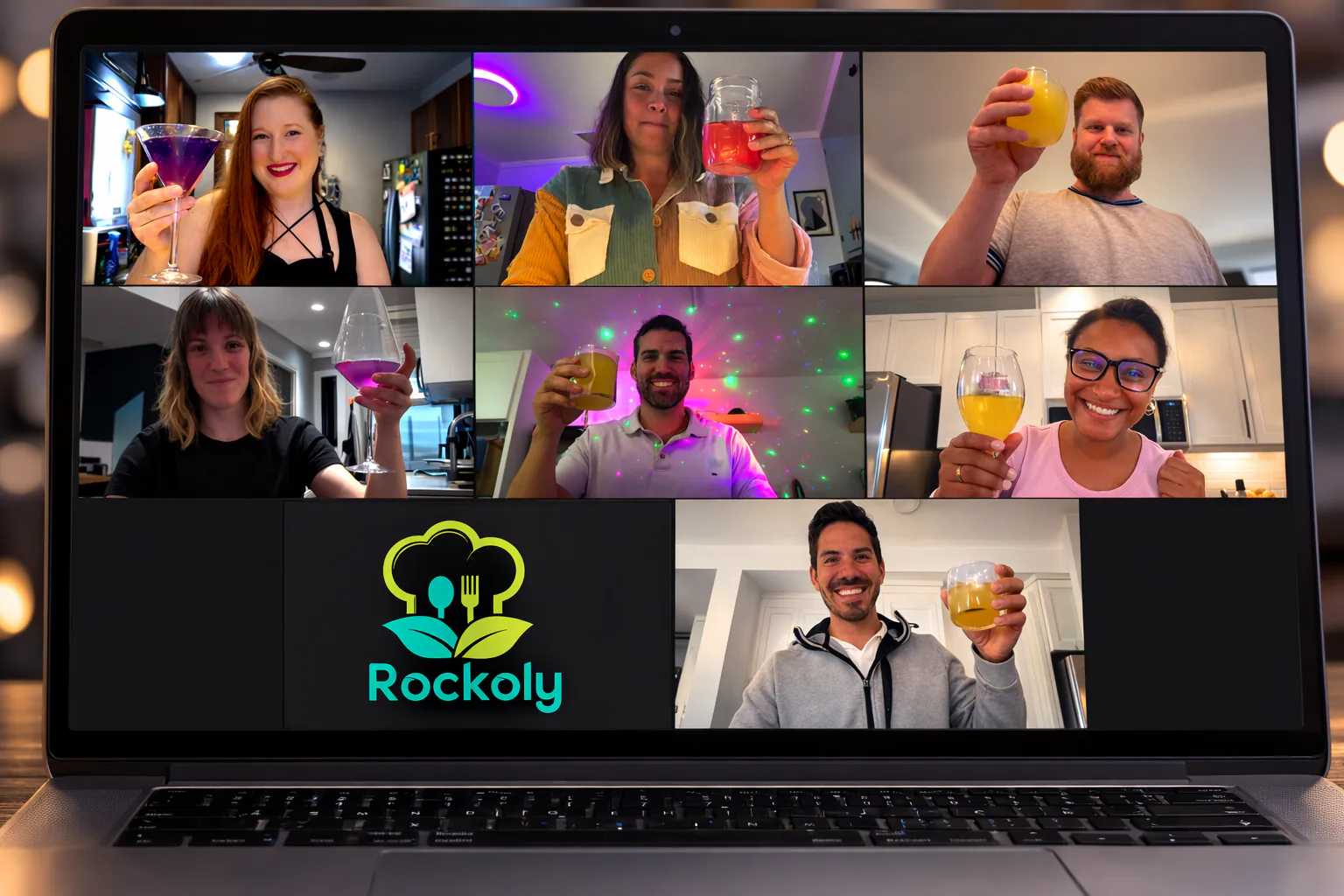 Laptop showing a video call of seven people raising colorful cocktails, with a Rockoly logo tile