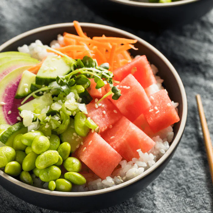 Poke bowl of sushi rice topped with cubed watermelon, edamame, shredded carrot, cucumber and sesame