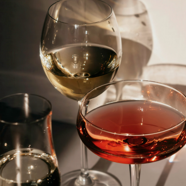 Glass of white wine, a coupe of red cocktail and a tumbler catching soft light