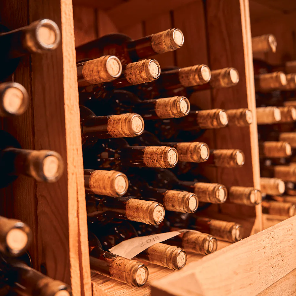 Corked wine bottles resting on their sides in a wooden cellar rack