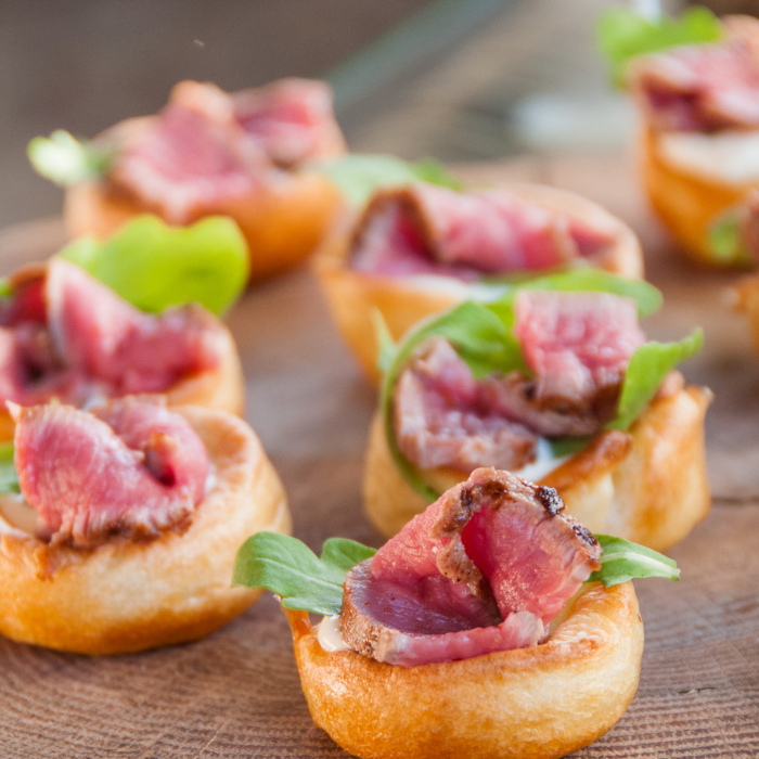 Yorkshire pudding bites topped with rare roast beef and arugula on a wooden board
