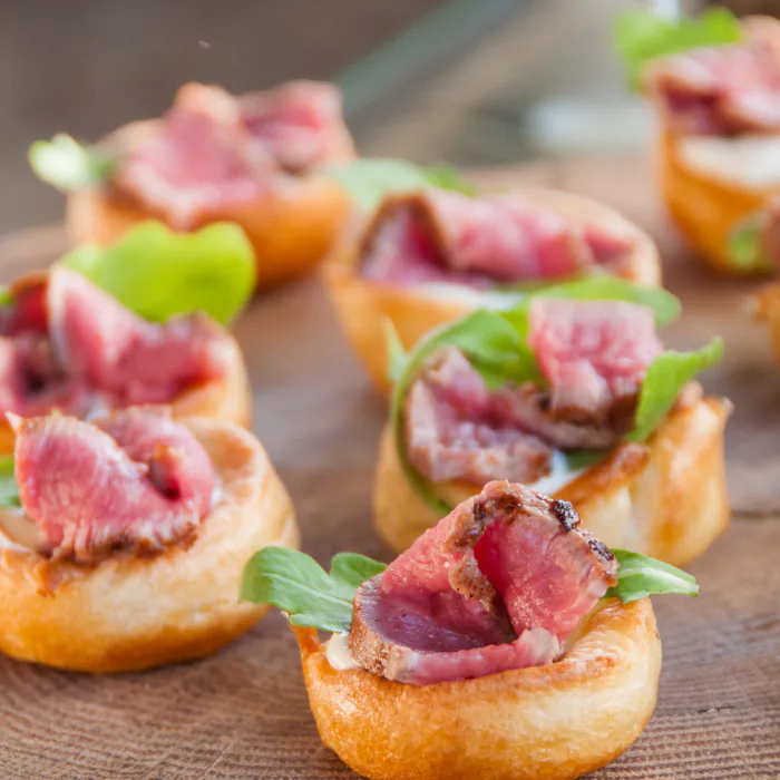 Yorkshire pudding bites topped with rare roast beef and arugula on a wooden board
