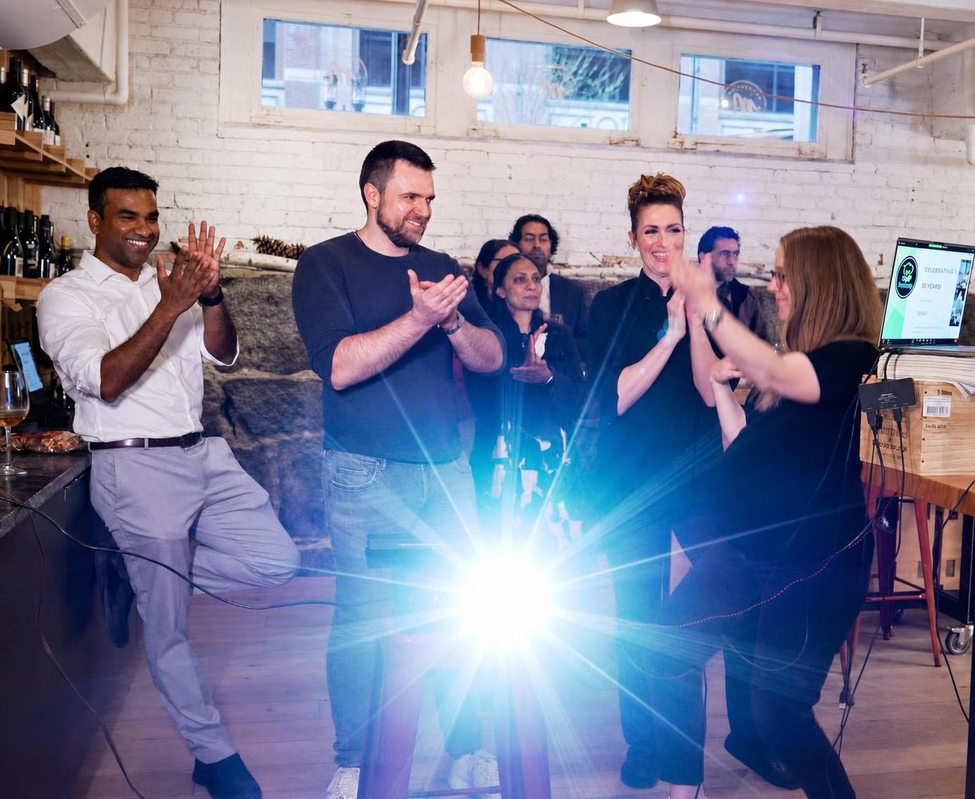 Colleagues clapping and cheering during a live team event in a brick-walled loft space