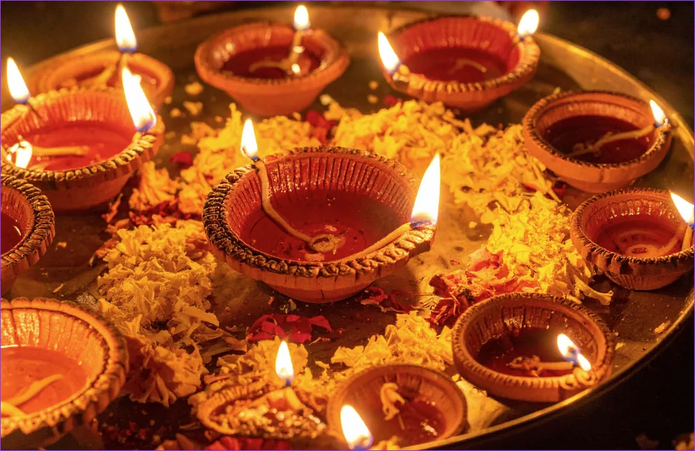 Diya oil lamps are lit and arranged on a tray with flower petals and garnishments around them