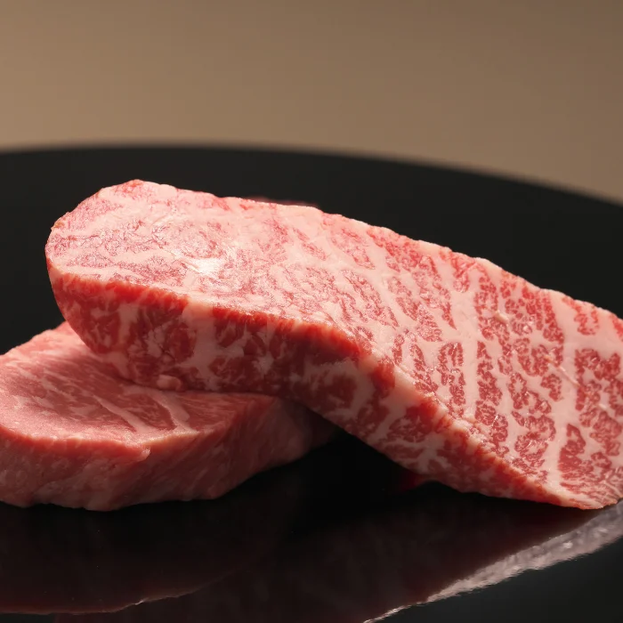 Two thick cuts of heavily marbled raw wagyu beef resting on a dark plate