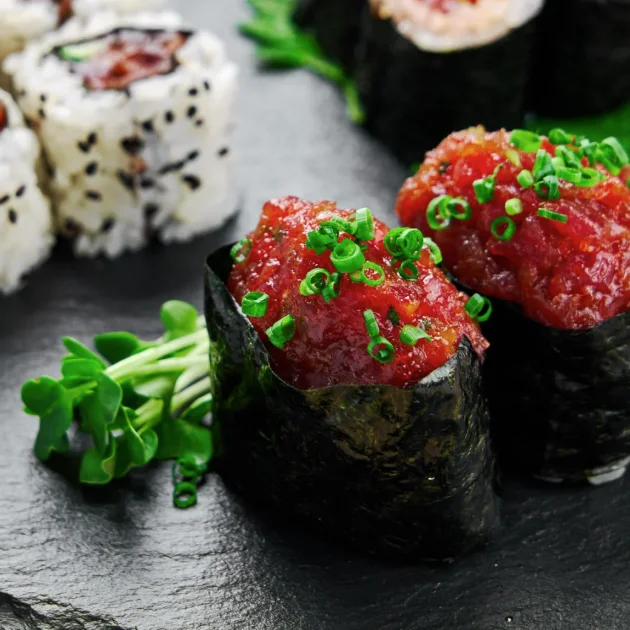 Close-up of nori-wrapped sushi topped with spicy tuna and sliced scallions on a slate board