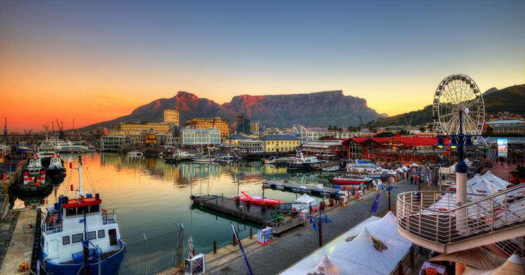 View of Cape Town, South Africa at sunset with mountains, ferris wheel, and boats 